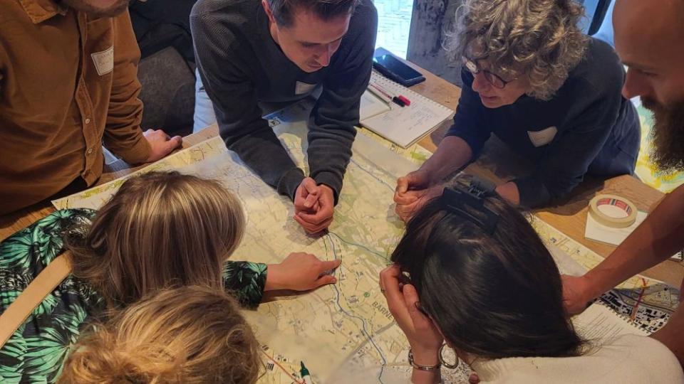 Deelnemers van het Leerwerktraject zitten gebogen over een tafel met een flipover en maken aantekeningen terwijl ze overleggen.